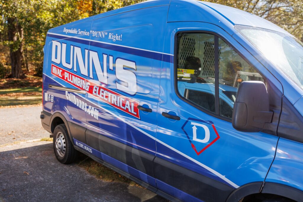 A blue Dunn's service van with HVAC, plumbing, and electrical branding is parked outside on a sunny Oxford day.