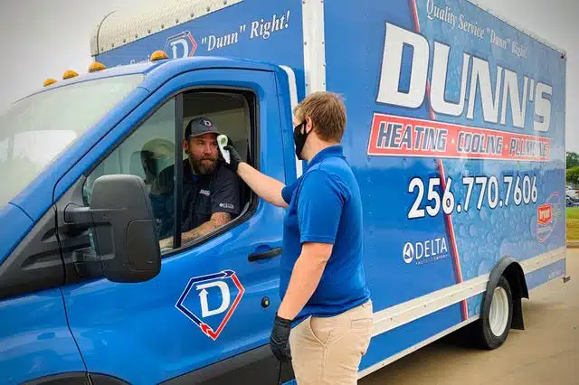 A man in a blue shirt checks the temperature of a driver sitting in a Dunn’s Heating, Cooling & Plumbing van using a handheld device.