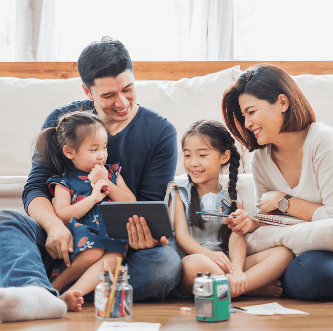 A family of four sits on the floor together, smiling and looking at a tablet with drawing supplies and a camera in front of them, perfectly capturing the warmth and creativity behind our "about us" story.