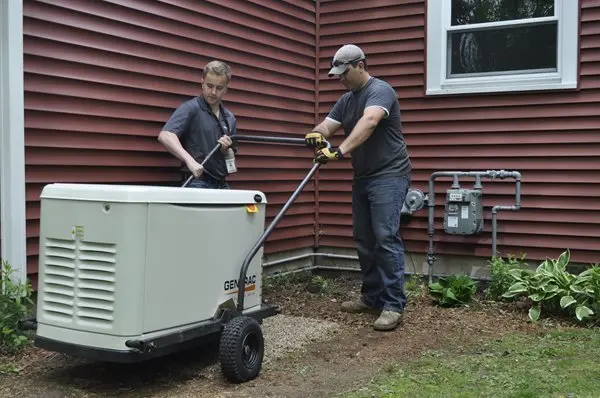 Two men are installing a portable generator next to the exterior wall of a house with red siding.
